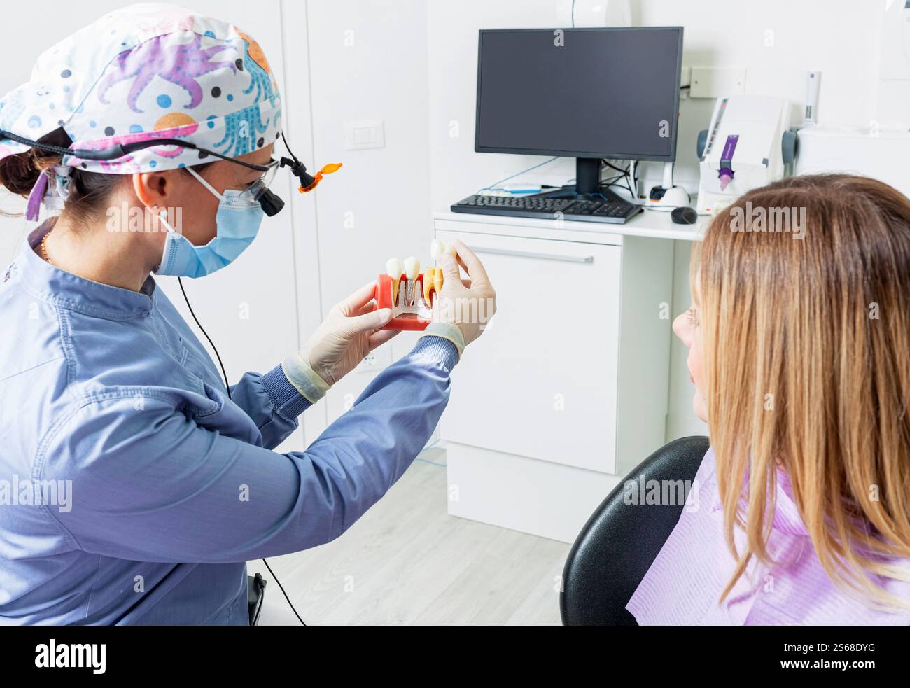 Femme dentiste expliquant la procédure d'implant dentaire à la patiente à l'aide d'un modèle anatomique en clinique moderne Banque D'Images