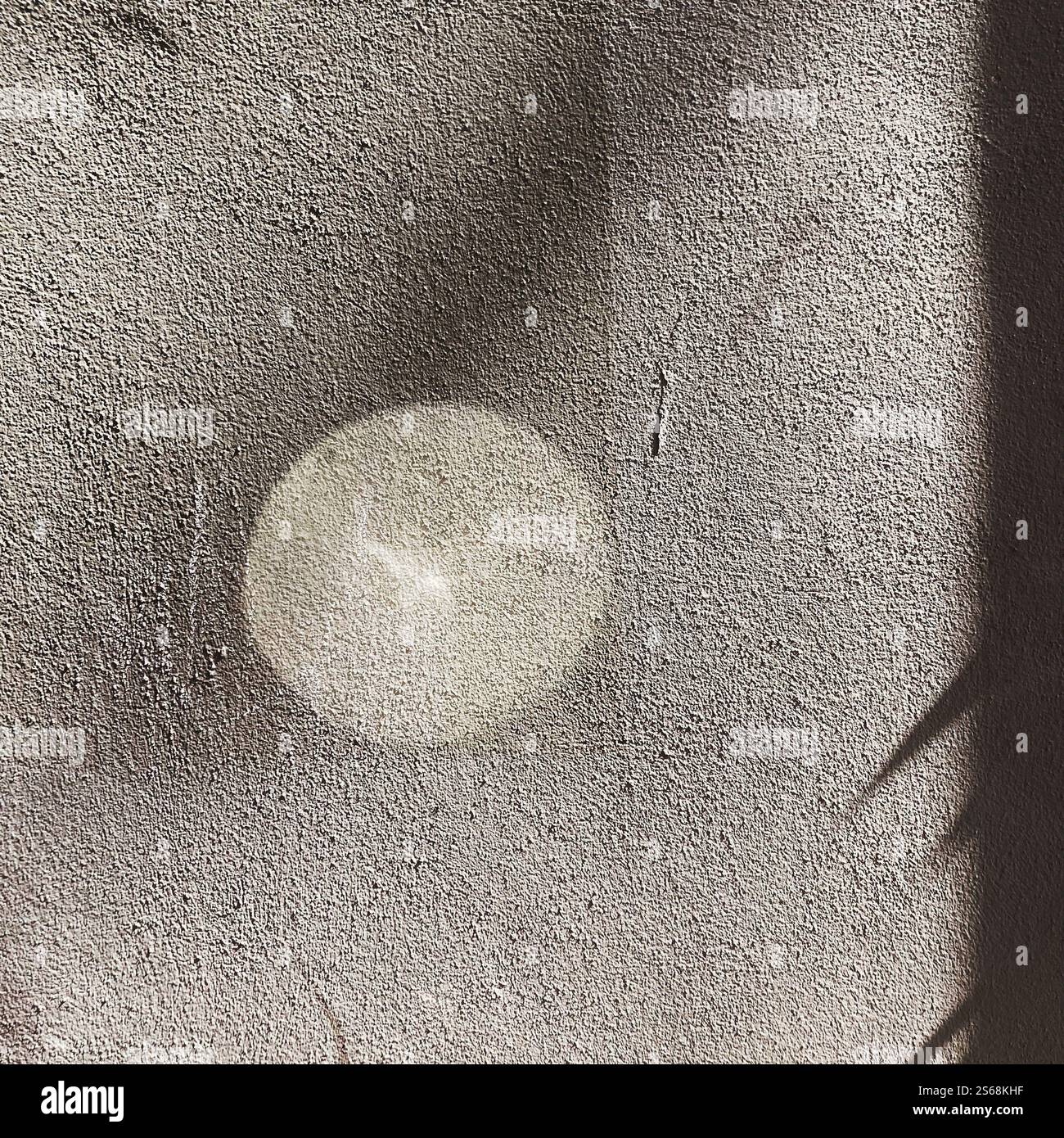 Composition abstraite de réflexion de la lumière créant une lueur circulaire sur le mur texturé, complétée par des ombres tendres, évoquant le calme. Banque D'Images