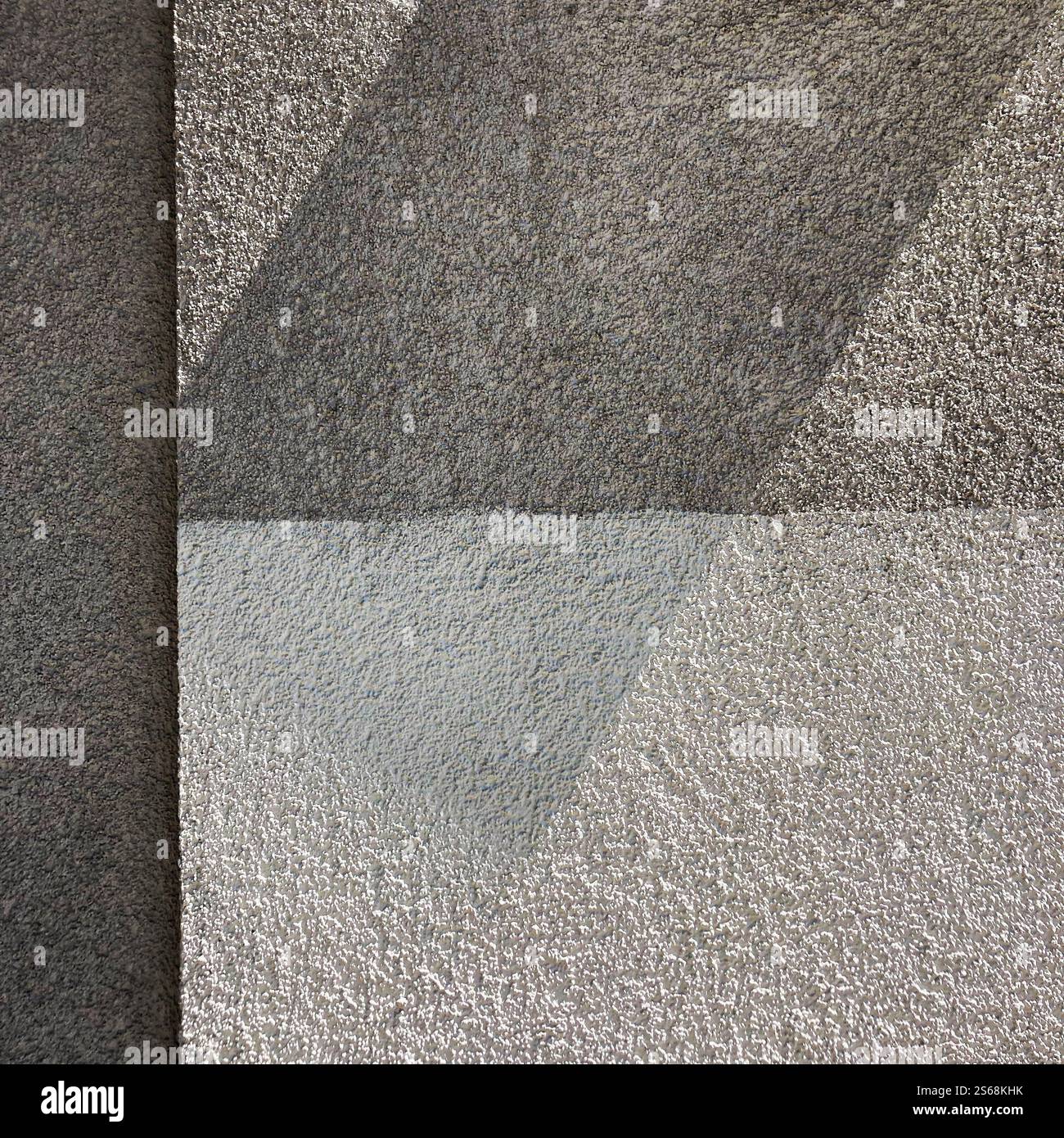 Gros plan d'un mur texturé montrant des formes géométriques abstraites dans des tons de gris avec une ombre rectangulaire tombant à travers. - Image de stock capturée avec un smartphone