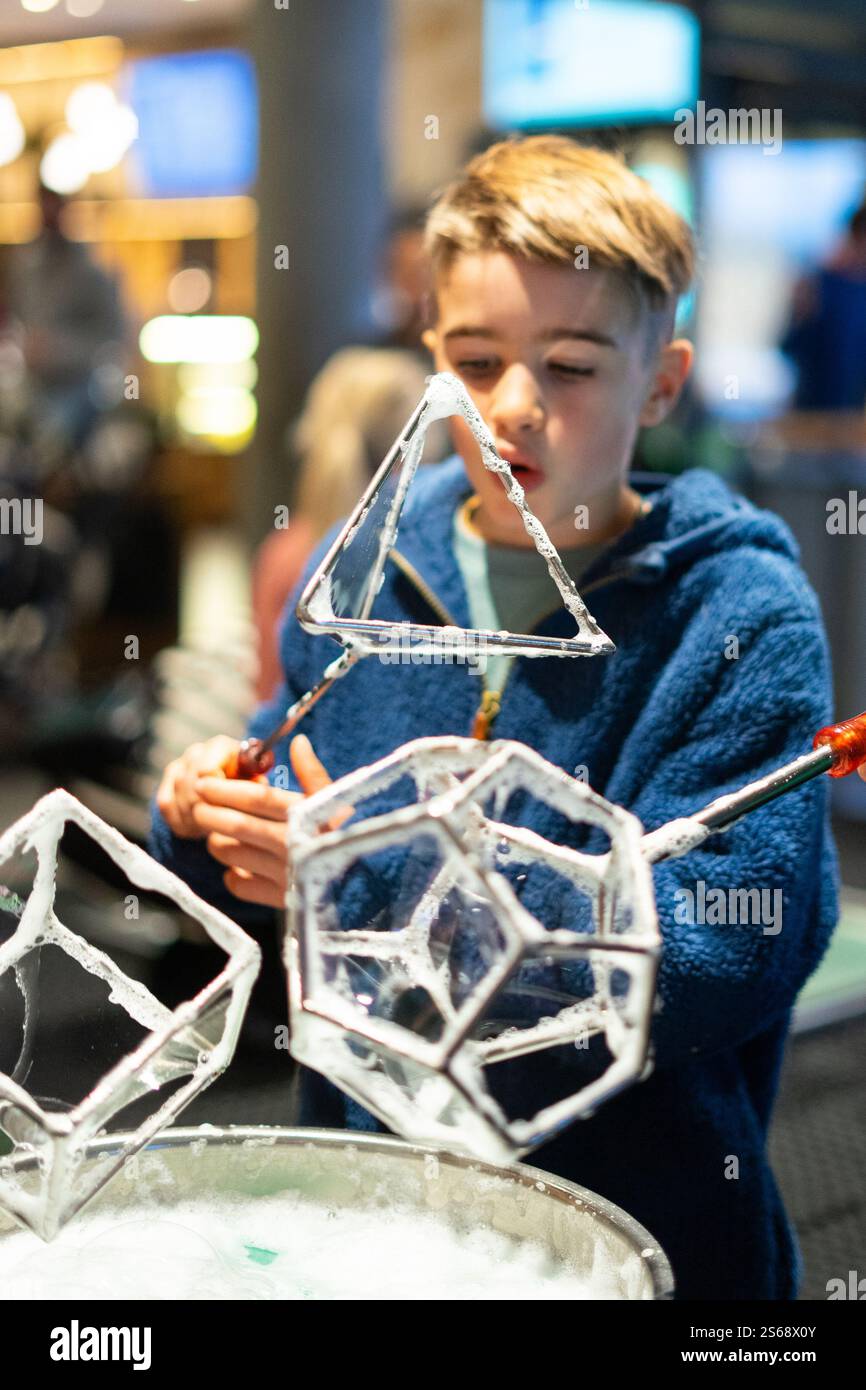 Enfant explorant la science et s'amusant à créer des bulles de savon géométriques avec des cadres métalliques dans un musée Banque D'Images