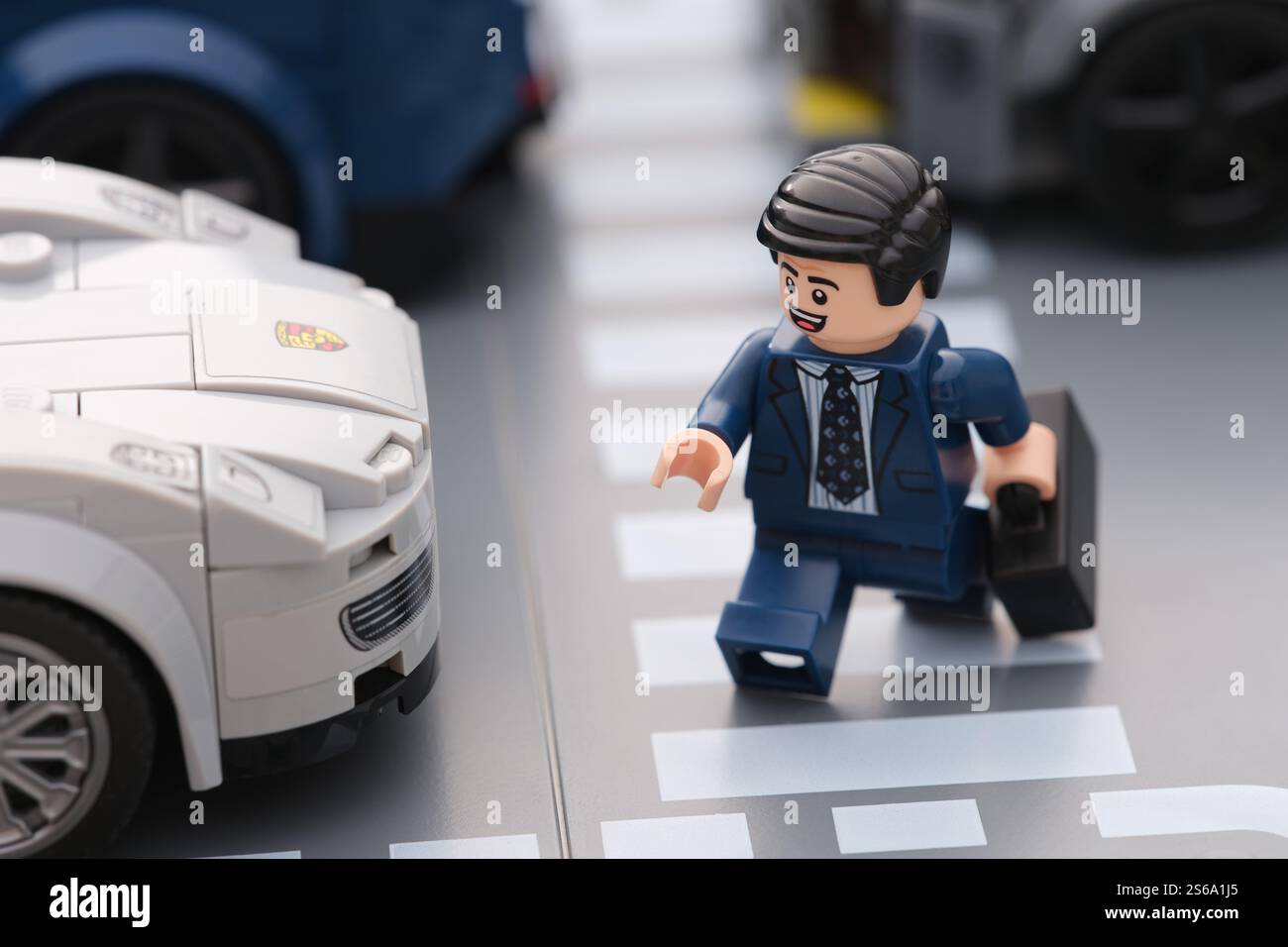 Tambov, Fédération de Russie - 15 janvier 2025 Un homme d'affaires heureux Lego minifigure traversant un passage piétonnier à travers une route très fréquentée. Banque D'Images
