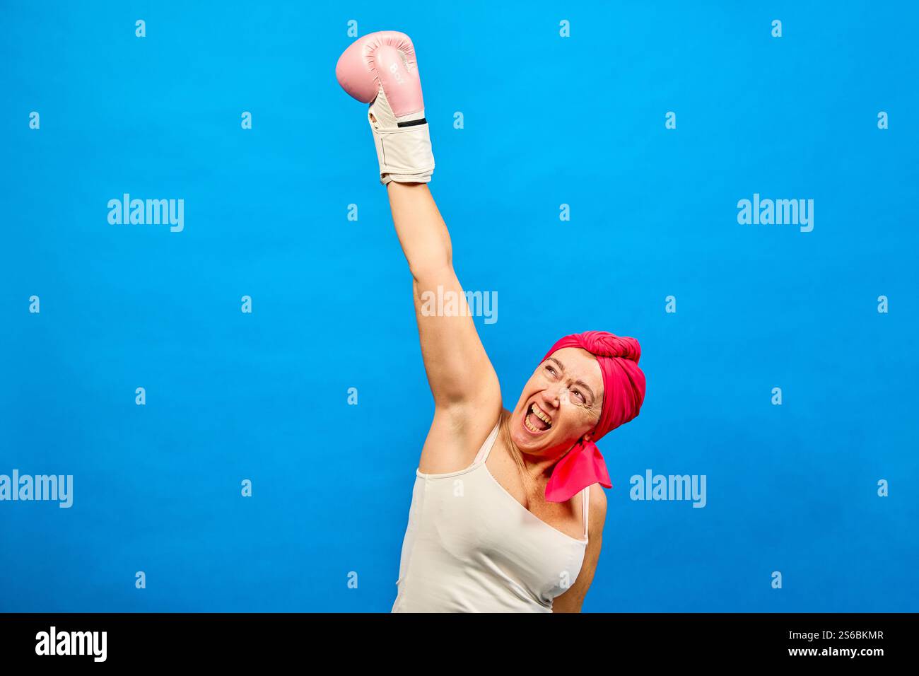 Forte femme d'âge moyen avec foulard rose levant le bras avec un gant de boxe, combattant le cancer et célébrant la victoire contre la maladie Banque D'Images
