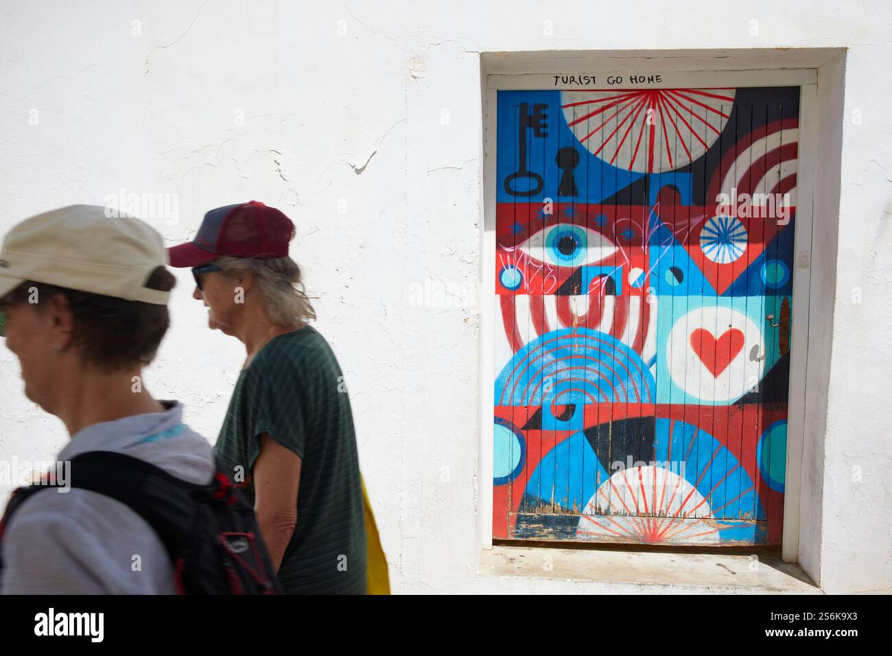 Touristes passant devant la porte peinte et Tourist Go Home graffiti sur la Calle Sant Miguel, Altea, Costa Blanca, Espagne Banque D'Images