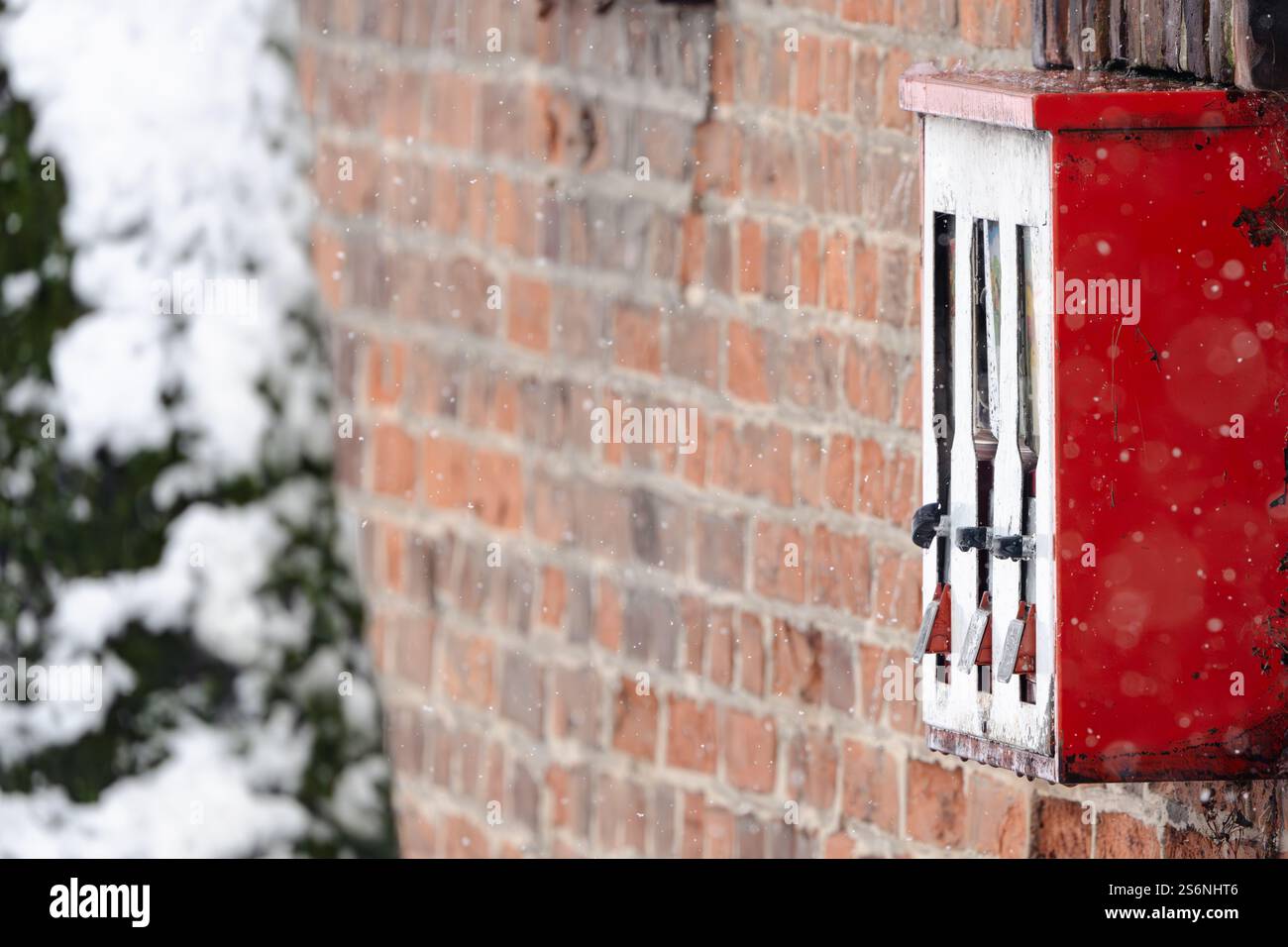 Un distributeur automatique rouge à trois compartiments est recouvert de neige. La neige tombe sur le bâtiment et la machine, créant un cadre paisible et serein Banque D'Images