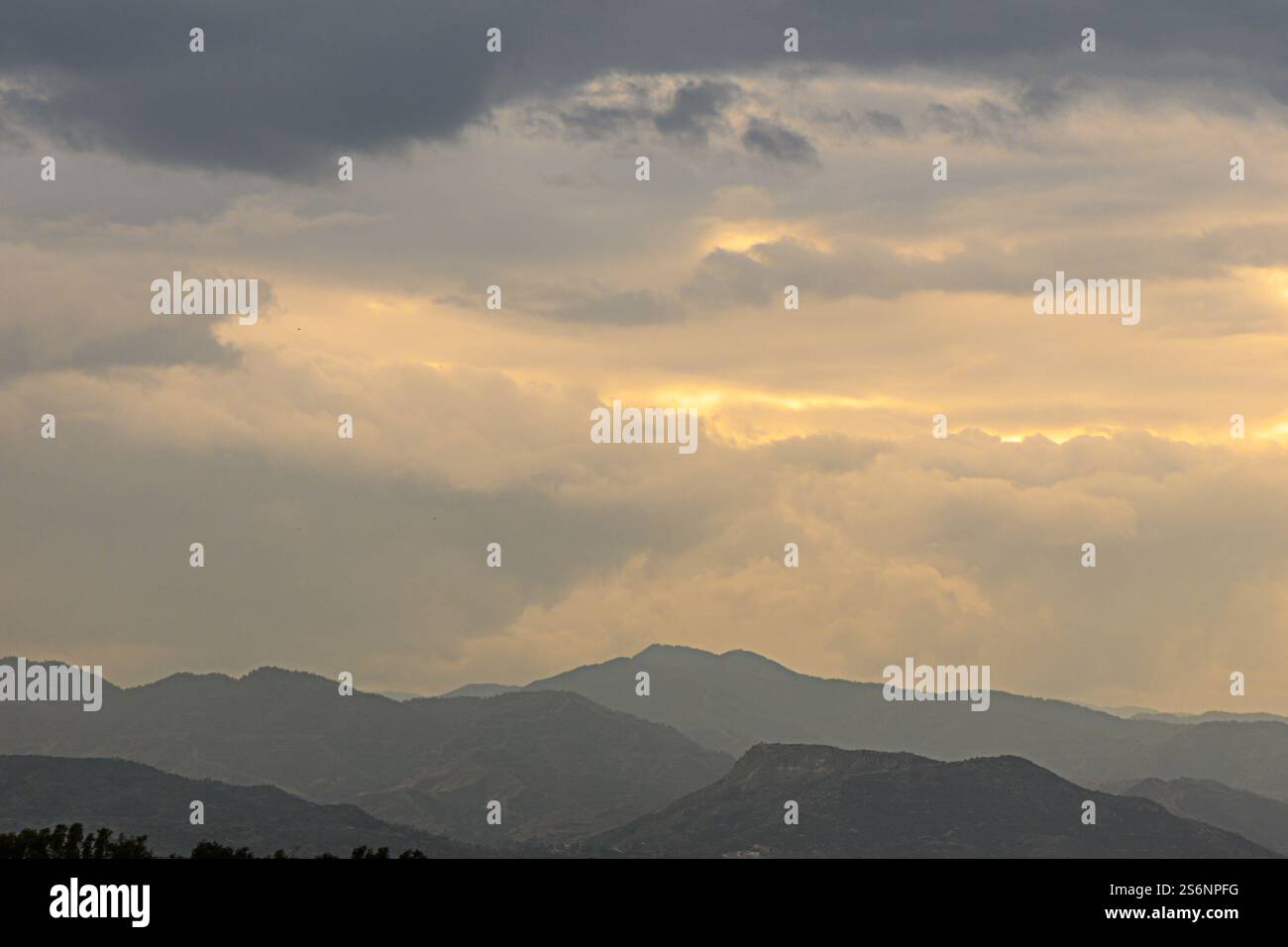 Les rayons dorés regardent à travers les nuages au-dessus des silhouettes montagneuses époustouflantes, créant une atmosphère tranquille et enchanteresse. Banque D'Images
