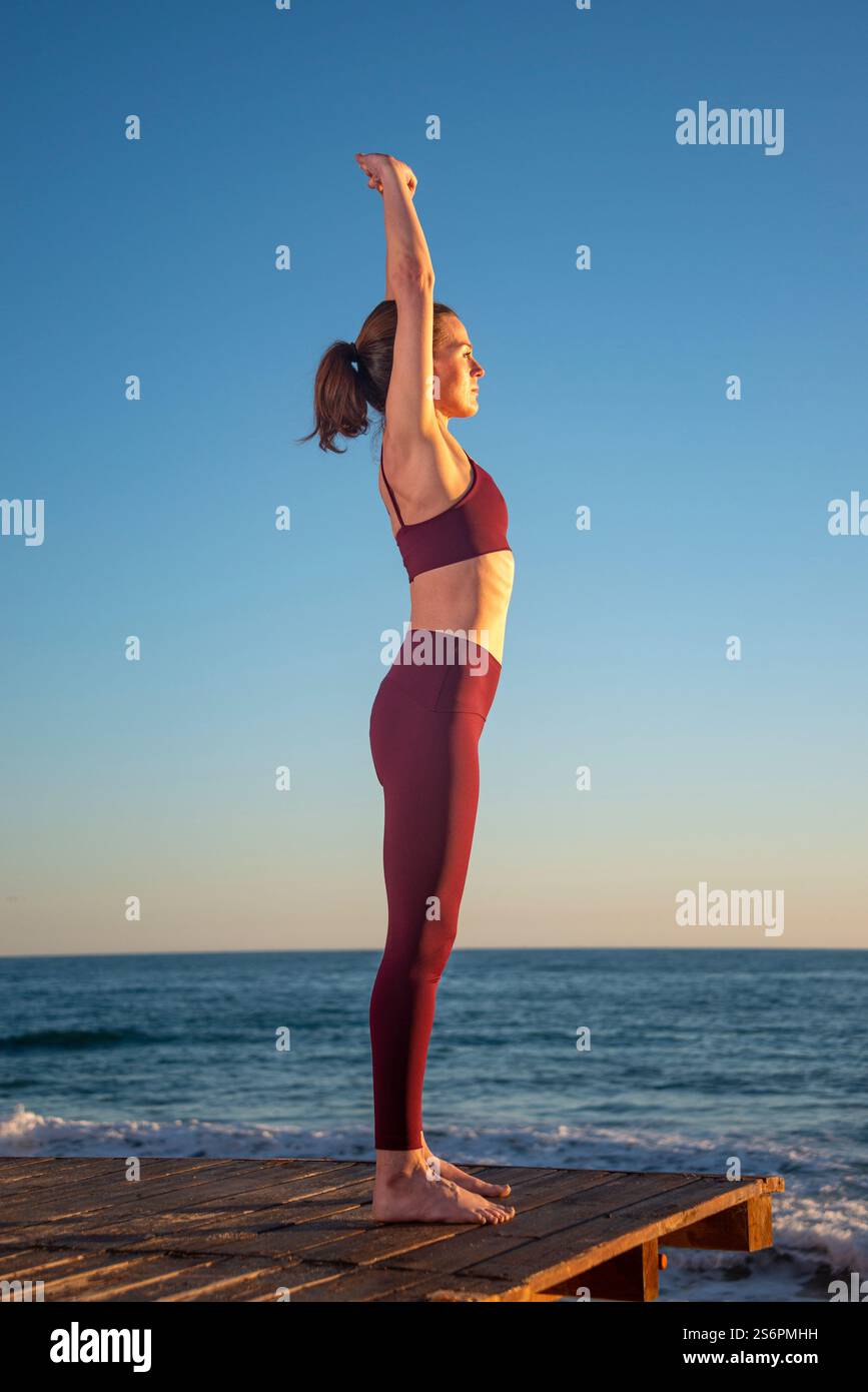 femme sportive faisant un exercice d'étirement avec les bras levés par la mer au lever du soleil au coucher du soleil Banque D'Images