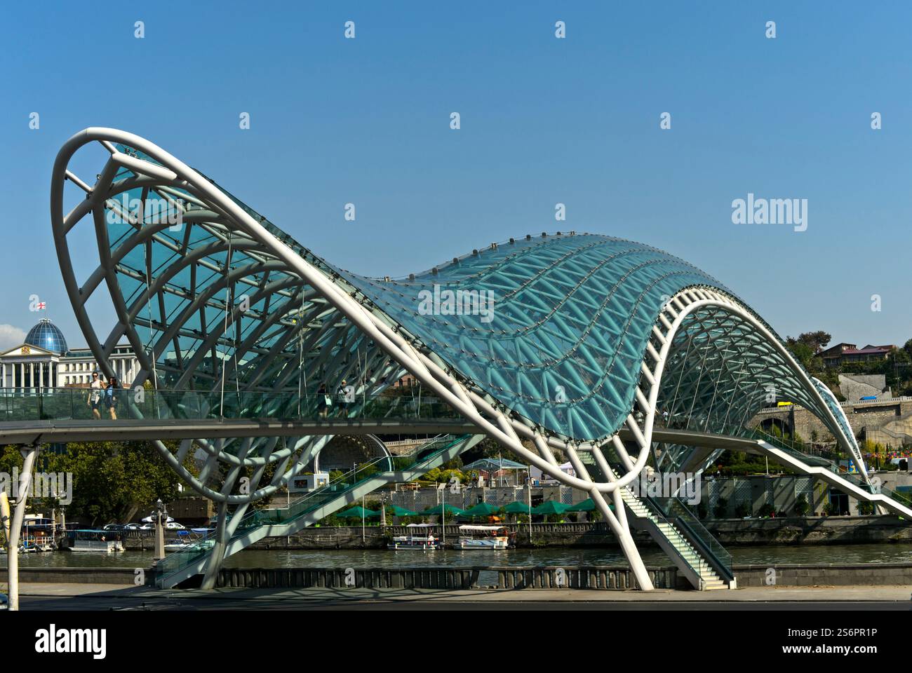 Le pont voûté futuriste de la paix sur la rivière Kura, architecte Michele de Lucci, derrière le Palais de Géorgie, anciennement le Palais présidentiel, Tbilissi, Géorgie Banque D'Images