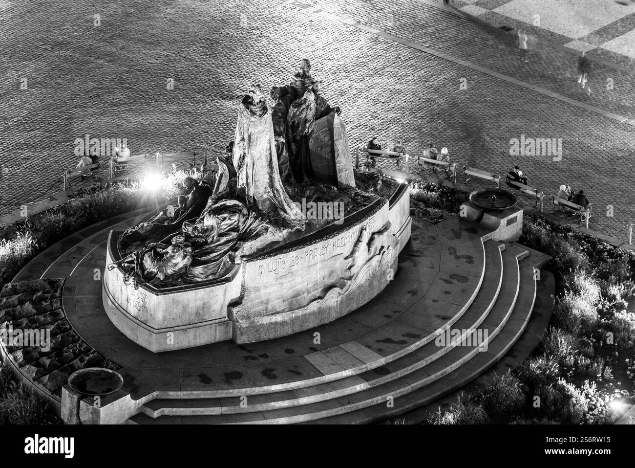 Le mémorial Jan Hus brille sous les lumières du soir sur la place de la vieille ville, Prague. Les visiteurs explorent la région, appréciant les détails frappants de ce monument historique. Banque D'Images