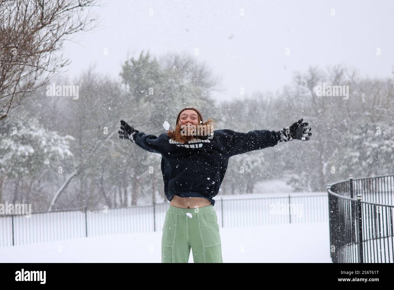 Une fille heureuse saute de joie, jouant joyeusement dans la chute de neige car il crée un pays des merveilles hivernales dans sa cour arrière avec des flocons de neige moelleux. Banque D'Images