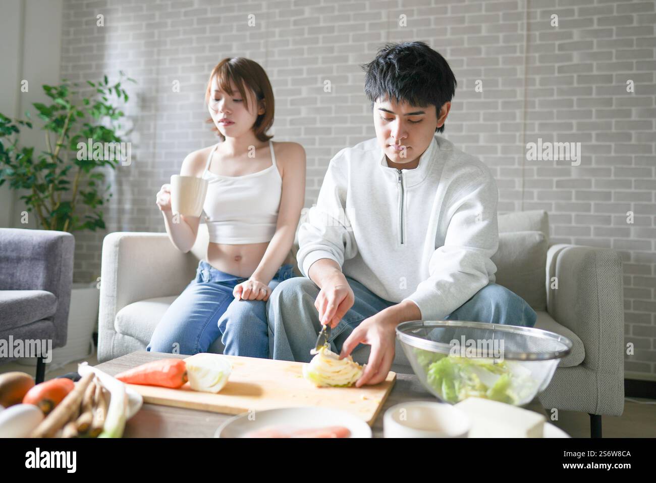 Une femme japonaise enceinte d'une vingtaine d'années et son mari, habillés pour montrer leur estomac, s'assoient sur un canapé dans un appartement. Banque D'Images