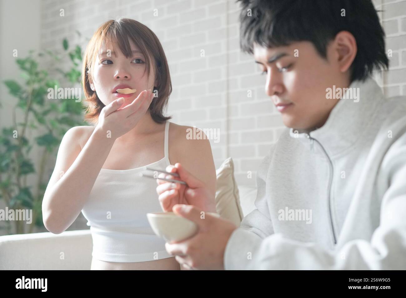 Une femme japonaise enceinte d'une vingtaine d'années et son mari, habillés pour montrer leur estomac, s'assoient sur un canapé dans un appartement. Banque D'Images