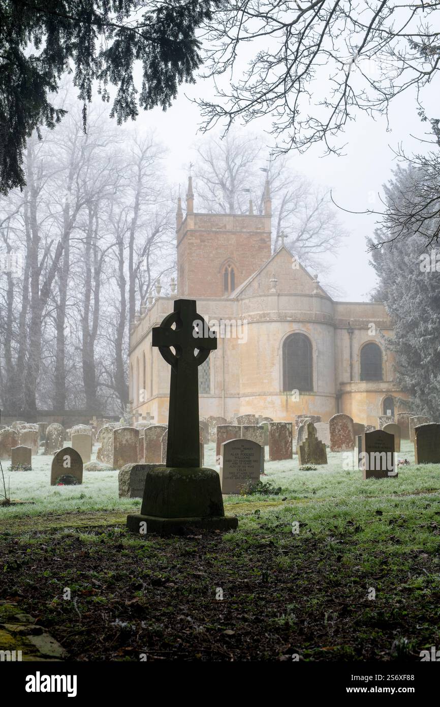 Croix de pierre dans le cimetière brumeux givré de l'église All Saints. Honington, Warwickshire, Angleterre Banque D'Images