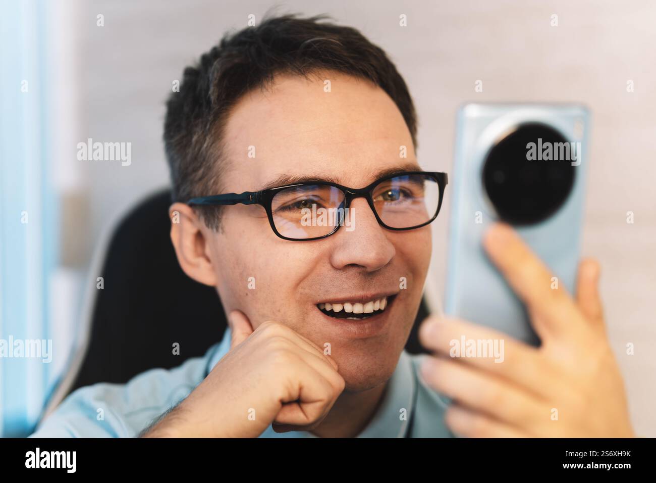 Heureux homme utilisant un smartphone à la maison, il discute messagerie en ligne sur mobile. Un jeune gars se repose dans le bureau et lit des informations d'un intelligent Banque D'Images