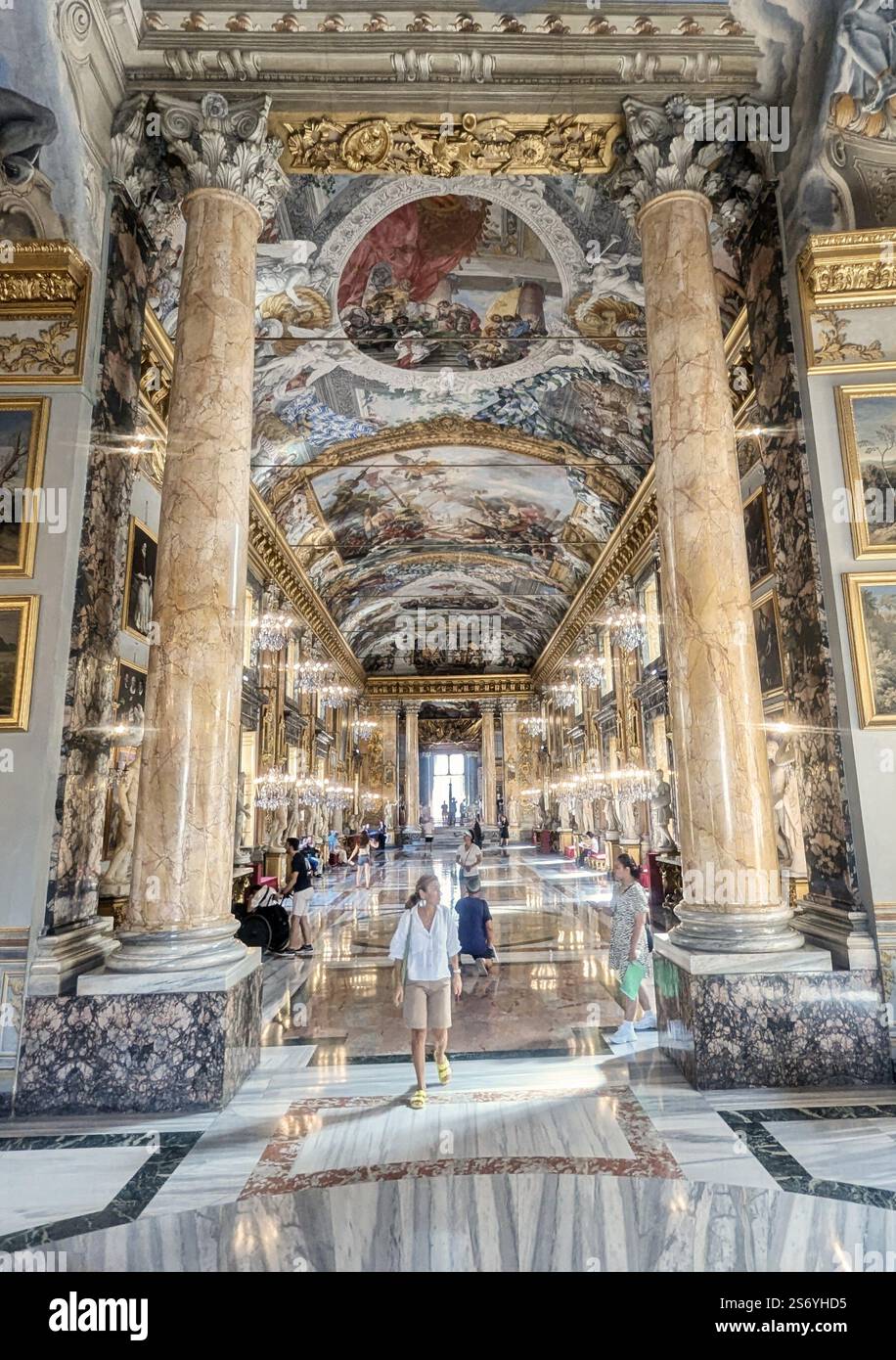 Un grand couloir avec des plafonds ornés de fresques, un décor doré et des colonnes de marbre, où les visiteurs admirent l'art opulent et l'élégance historique. - Image de stock capturée avec un smartphone