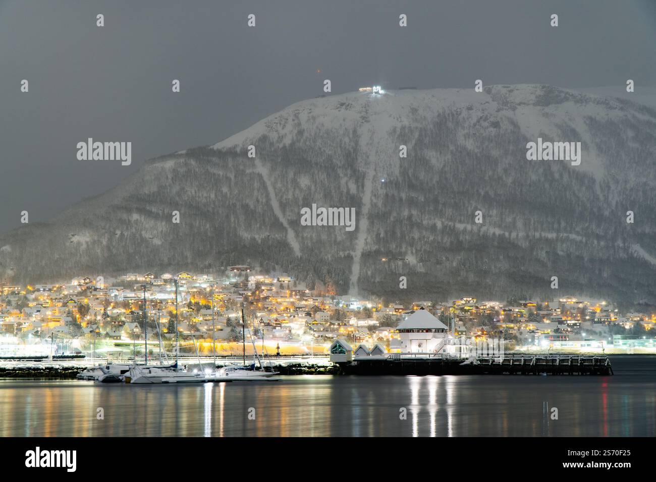 Vue nocturne de Tromsø avec des maisons illuminées et un front de mer du port devant le mont Storsteinen enneigé et le téléphérique de Fjellheisen, Norvège Banque D'Images