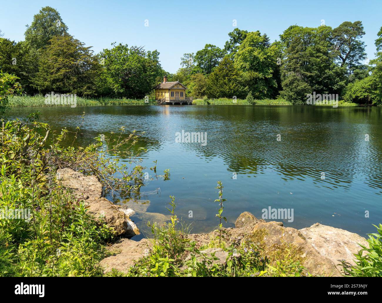 Belton House lac et hangar à bateaux sur une journée d'été ensoleillée en juin avec l'eau calme et le ciel bleu clair, Grantham, Lincolnshire, Angleterre, Royaume-Uni Banque D'Images