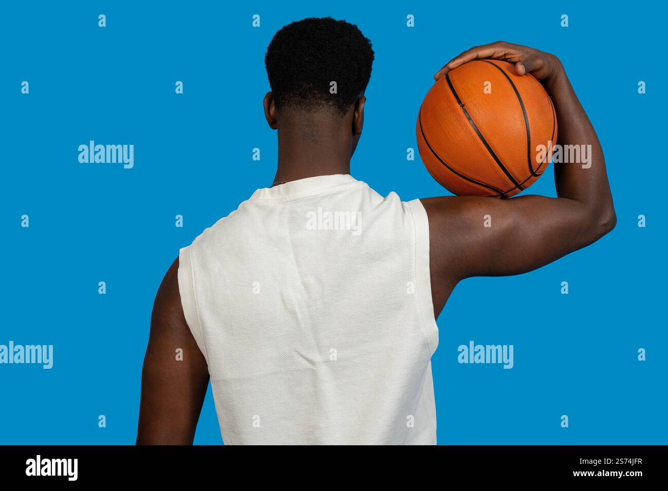 Vue arrière d'un joueur de basket-ball tenant une balle sur son épaule, prêt pour l'action sur un fond bleu Banque D'Images