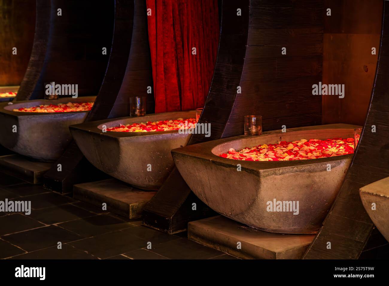 Intérieur faiblement éclairé d'un spa de luxe avec trois baignoires en pierre remplies d'eau et de pétales de fleurs de rose, créant une ambiance relaxante et intime Banque D'Images