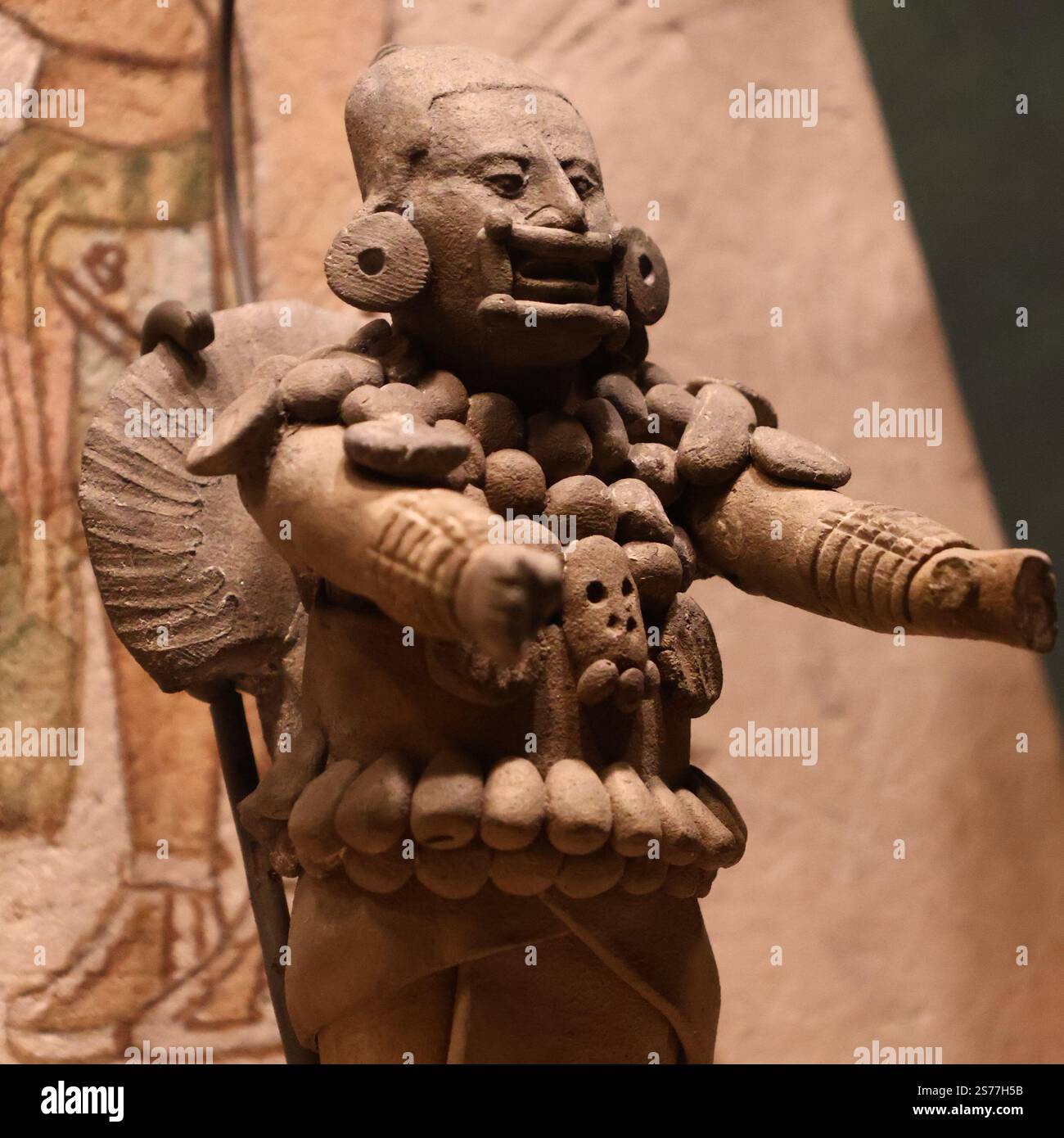 Ancienne figurine en céramique méso-américaine d'un guerrier debout ou noble, probablement de la culture maya ou zapotèque. La figure porte une coiffe ornée d'un motif animal, un collier de perles et une tenue traditionnelle. Bras croisés, symbolisant le pouvoir et le statut. Artefact précolombien. Banque D'Images