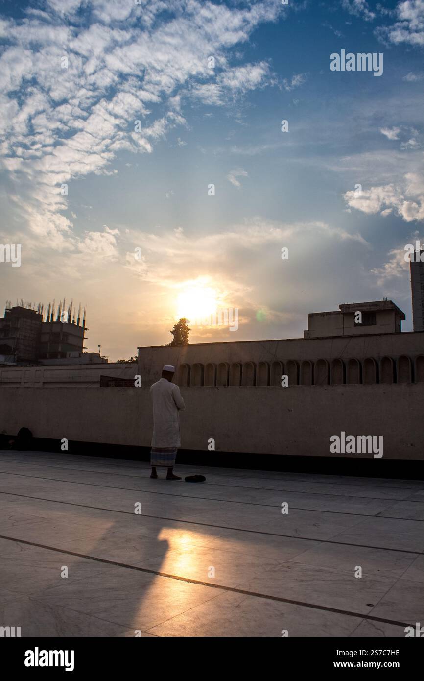 Un homme priant à la mosquée nationale Baitul Mukarram à Dhaka, au Bangladesh, baigné dans la lueur chaude de la belle lumière du soleil contre un ciel serein. Banque D'Images