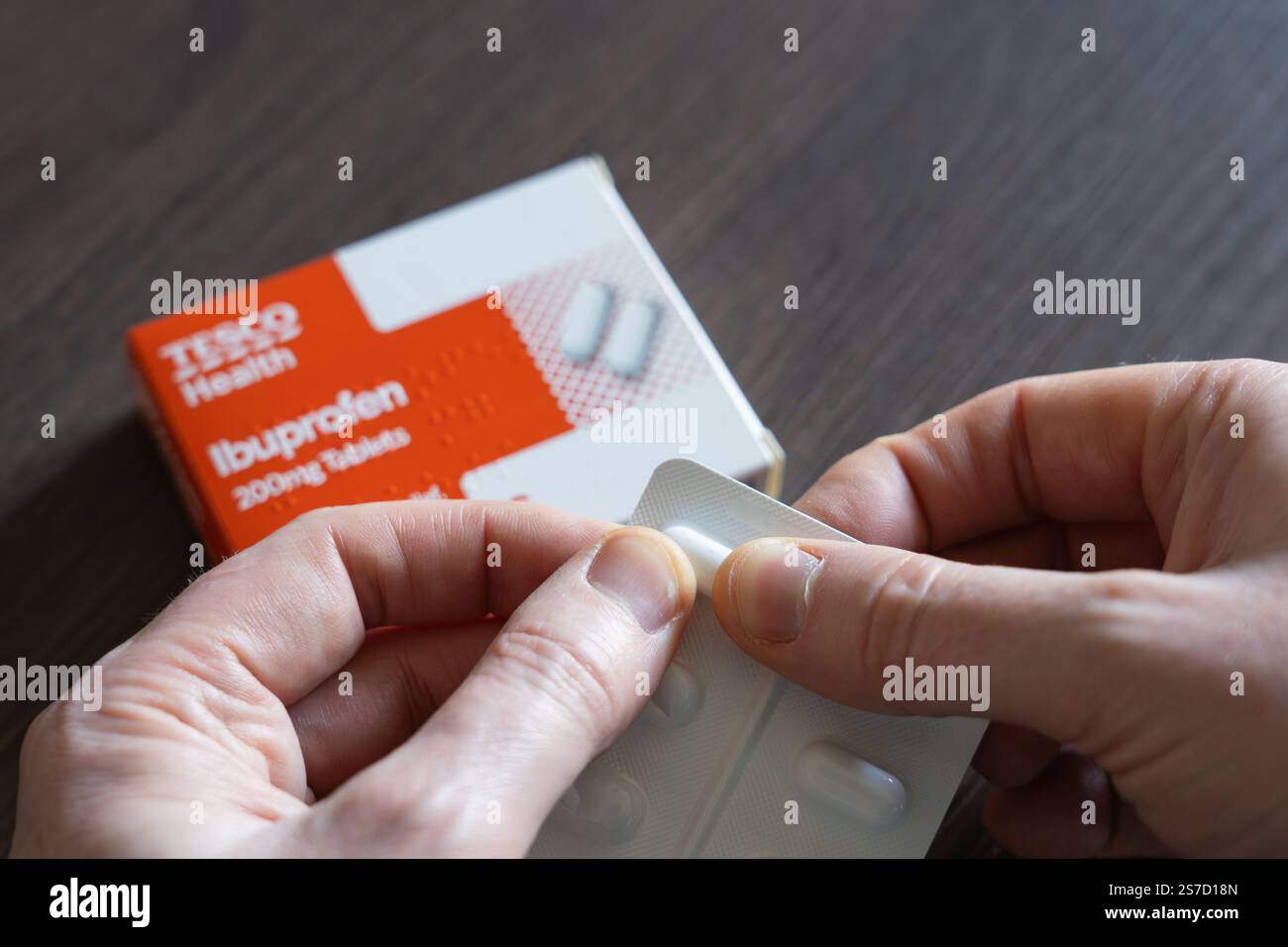 Homme d’âge moyen retrait d’un comprimé d’ibuprofène d’une plaquette thermoformée. Avec boîte de marque Tesco Health & utilisé pour soulager la douleur, la fièvre et l'inflammation. ROYAUME-UNI Banque D'Images