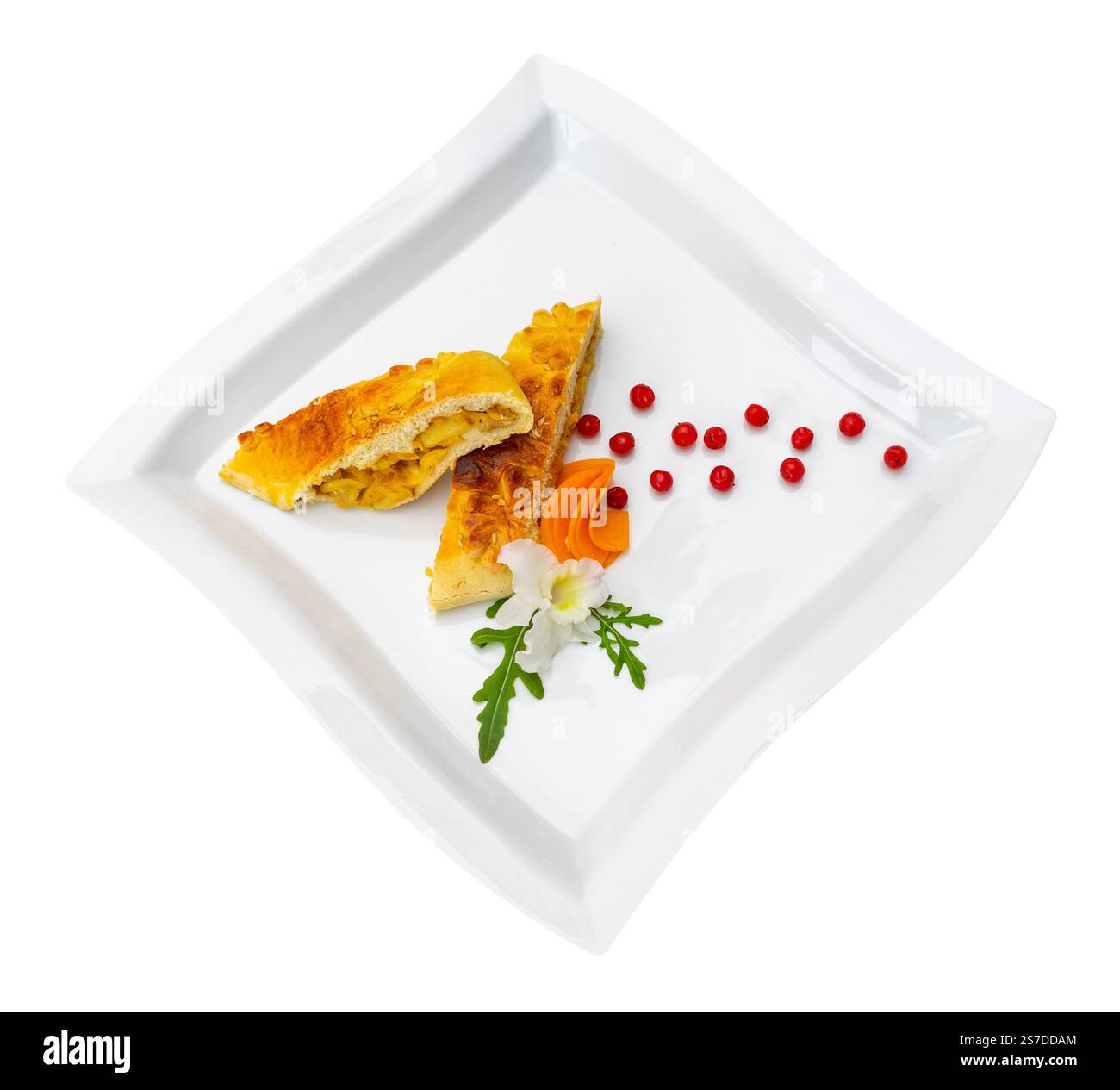 La pâtisserie salée repose élégamment sur une assiette blanche, accompagnée de garnitures colorées comme des boucles de carottes et des baies rouges. La présentation met en évidence le di Banque D'Images