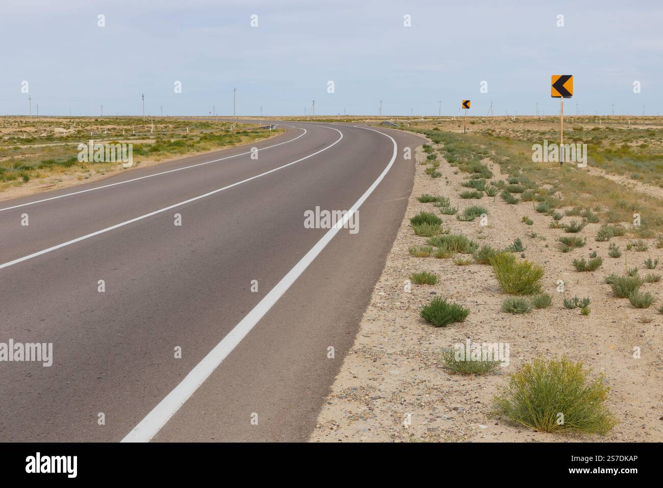 Une route sinueuse traverse le vaste terrain de la région de Mangystau au Kazakhstan, entourée d'une végétation clairsemée et d'un ciel ouvert. Banque D'Images