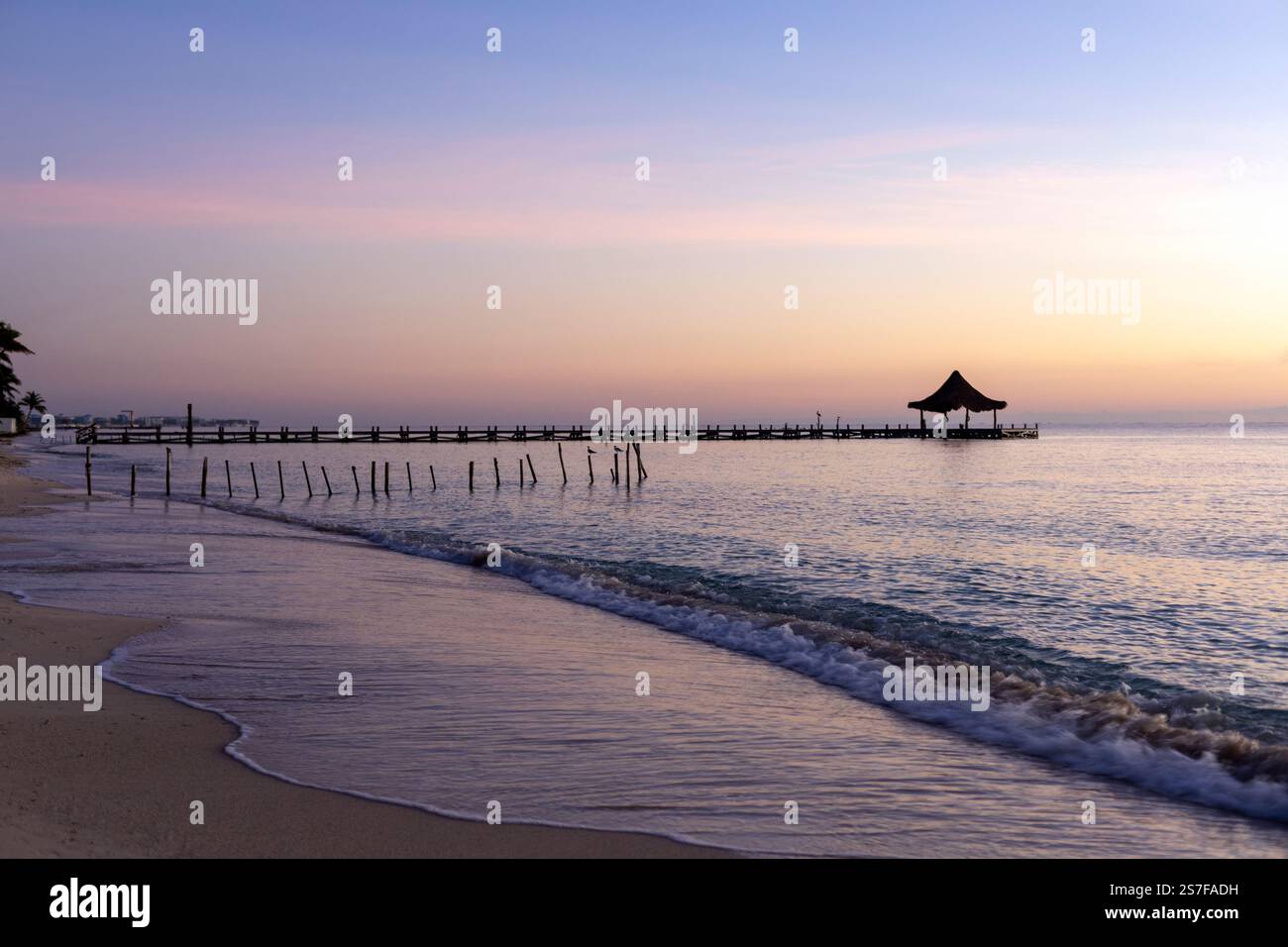 Mexique, Puerto Morelos, Pier avec palapa au lever du soleil sur une plage tranquille. Banque D'Images