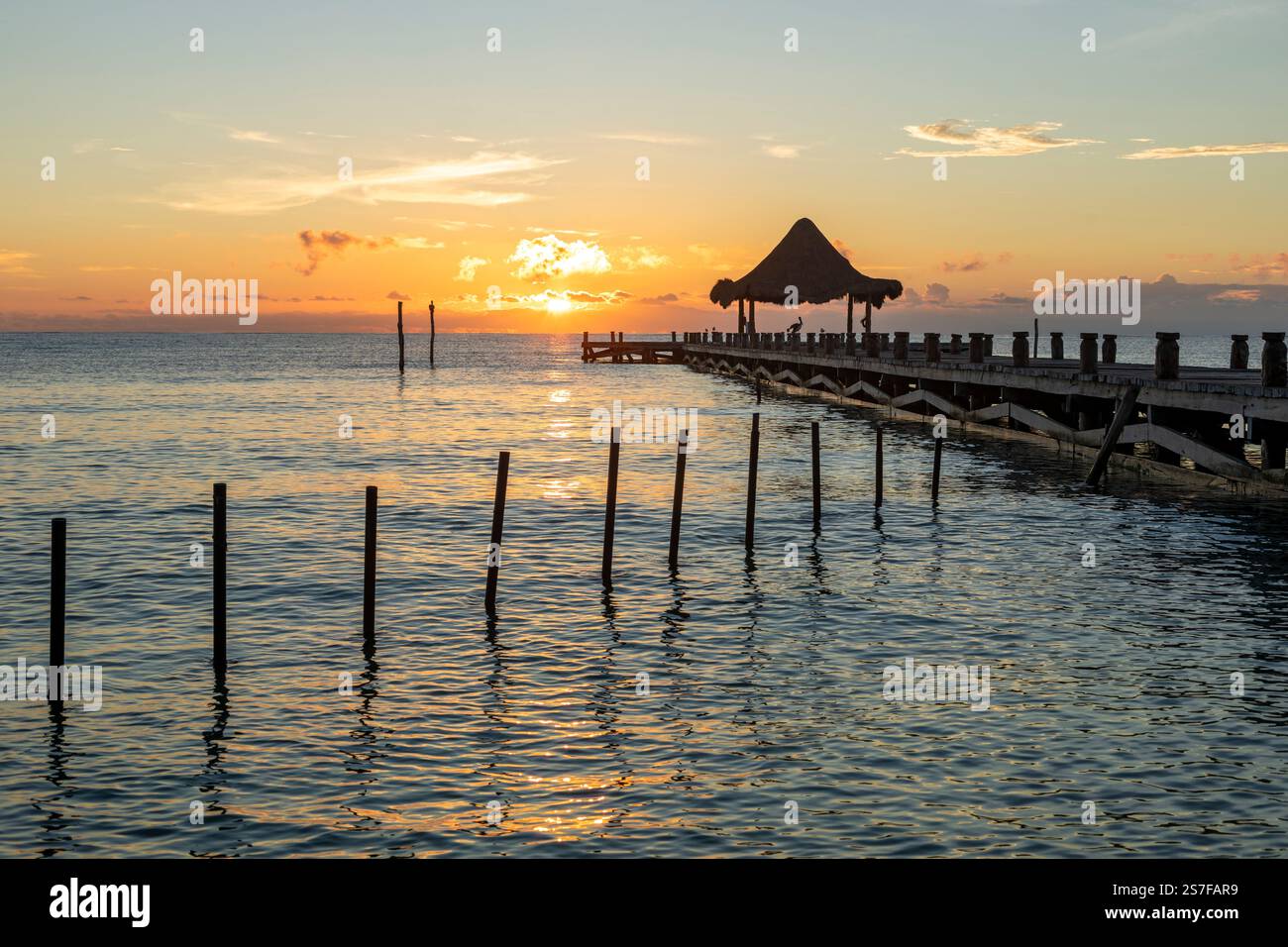 Mexique, Puerto Morelos, Pier avec palapa au lever du soleil sur une plage tranquille. Banque D'Images