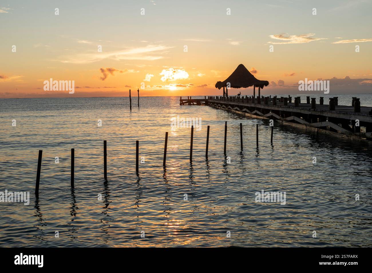 Mexique, Puerto Morelos, Pier avec palapa au lever du soleil sur une plage tranquille. Banque D'Images
