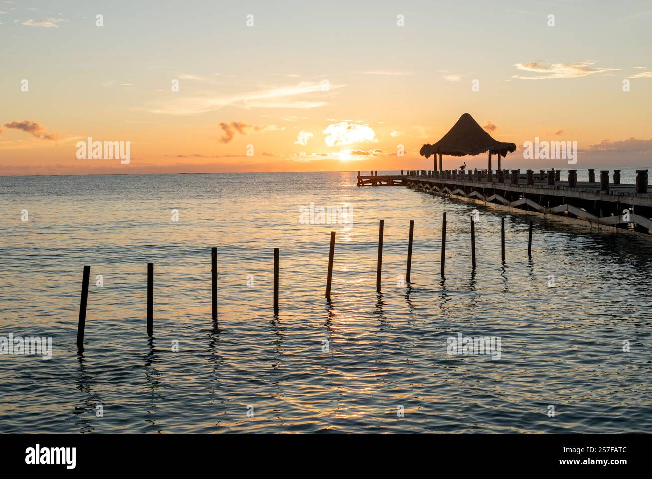Mexique, Puerto Morelos, Pier avec palapa au lever du soleil sur une plage tranquille. Banque D'Images
