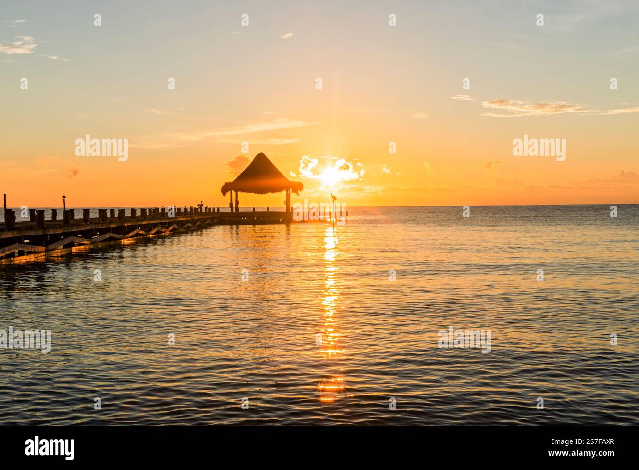 Mexique, Puerto Morelos, lever de soleil sur une plage avec une jetée et palapa, Banque D'Images