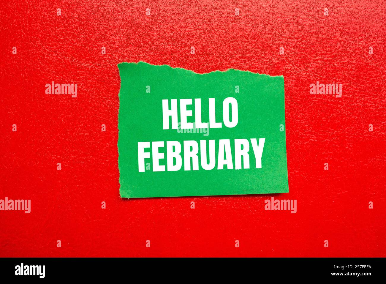 Bonjour février message écrit sur un morceau de papier vert déchiré déchiré avec fond rouge. Symbole conceptuel bonjour février. Copier l'espace. Banque D'Images