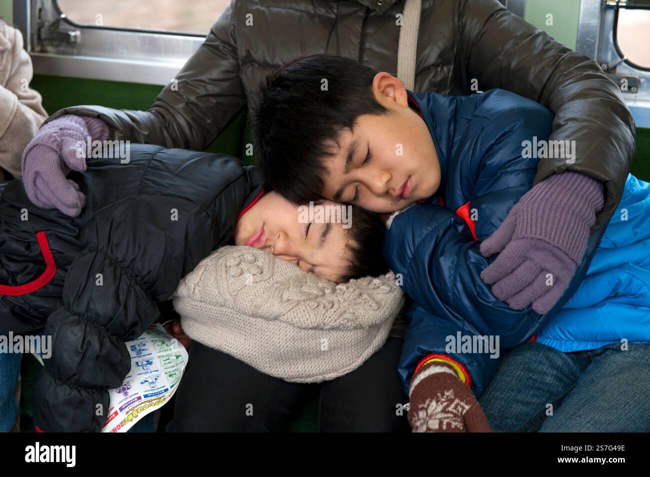 Deux frères reposant leur tête sur les genoux de leur mère pour une scène comique mais attachante à bord d'un train de voyageurs au Japon. Banque D'Images