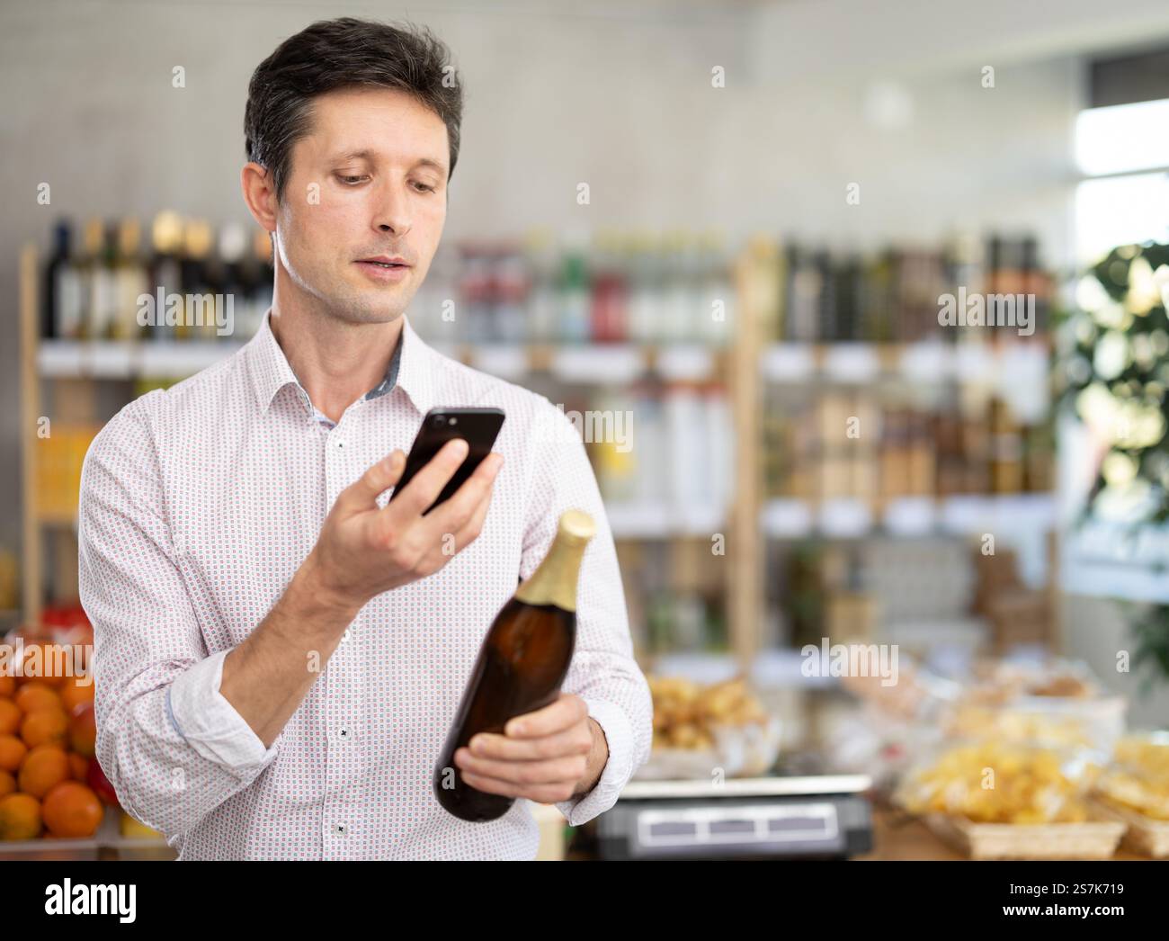 Homme en chemise légère scannez le code QR et prenez l'étiquette de la bière de lecture en utilisant la caméra du téléphone dans le magasin Banque D'Images