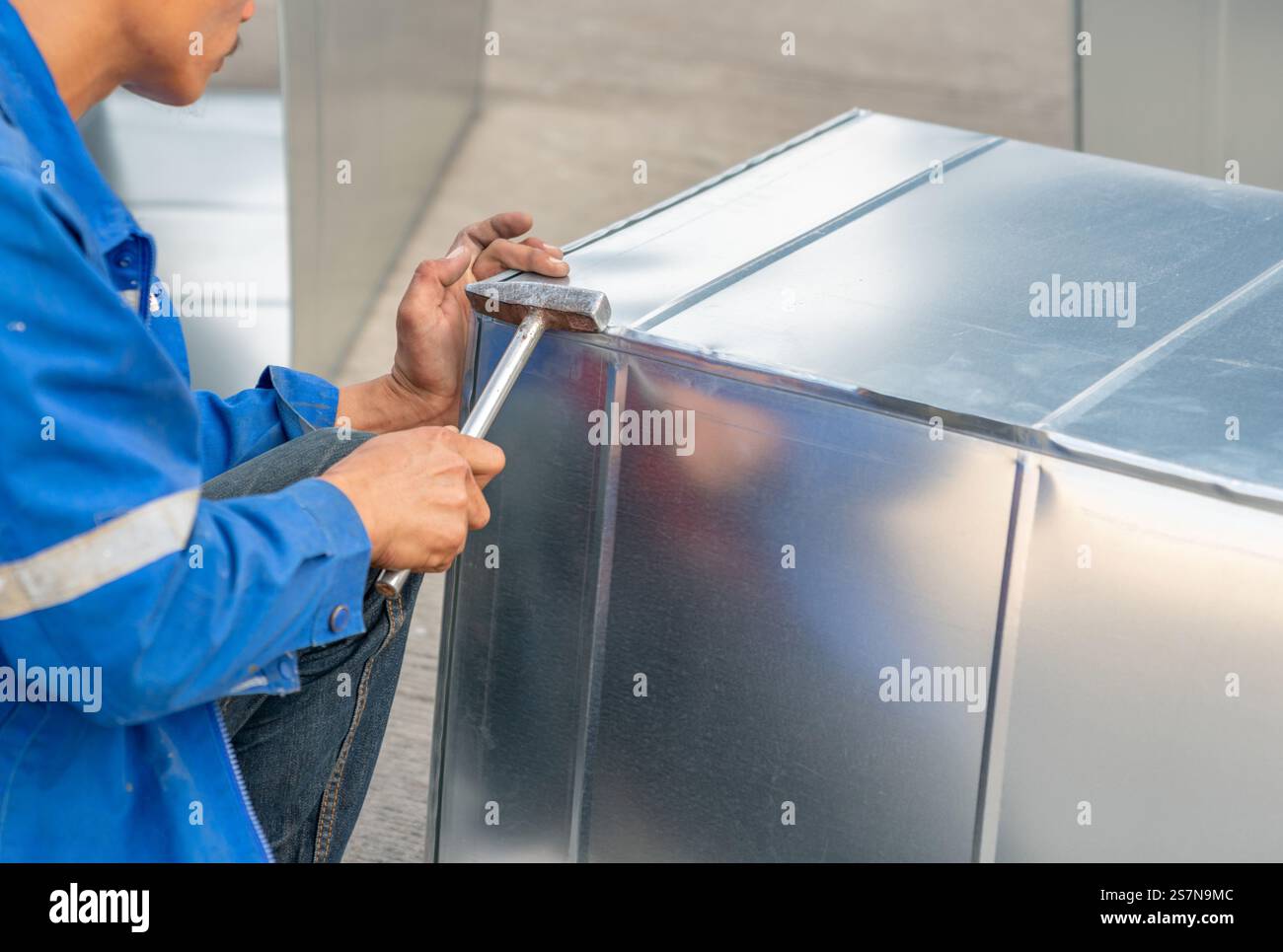 Technicien finissant le pliage d'un bord de tôle à l'aide d'un maillet métallique en atelier. Banque D'Images