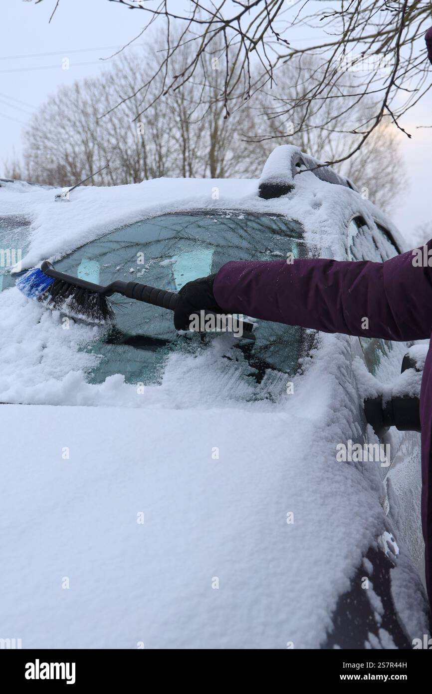 Jeune femme nettoyant la fenêtre de voiture de la neige tombée sous l'orientation verticale des branches Banque D'Images