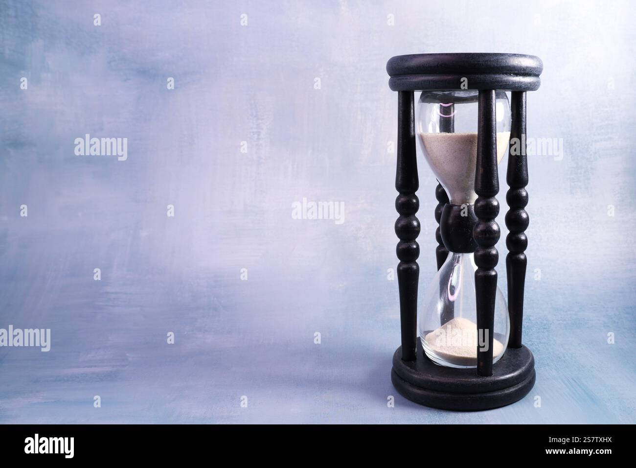 Minuterie de sable dans un cadre en bois noir avec supports décoratifs sur un BG bleu-gris Banque D'Images
