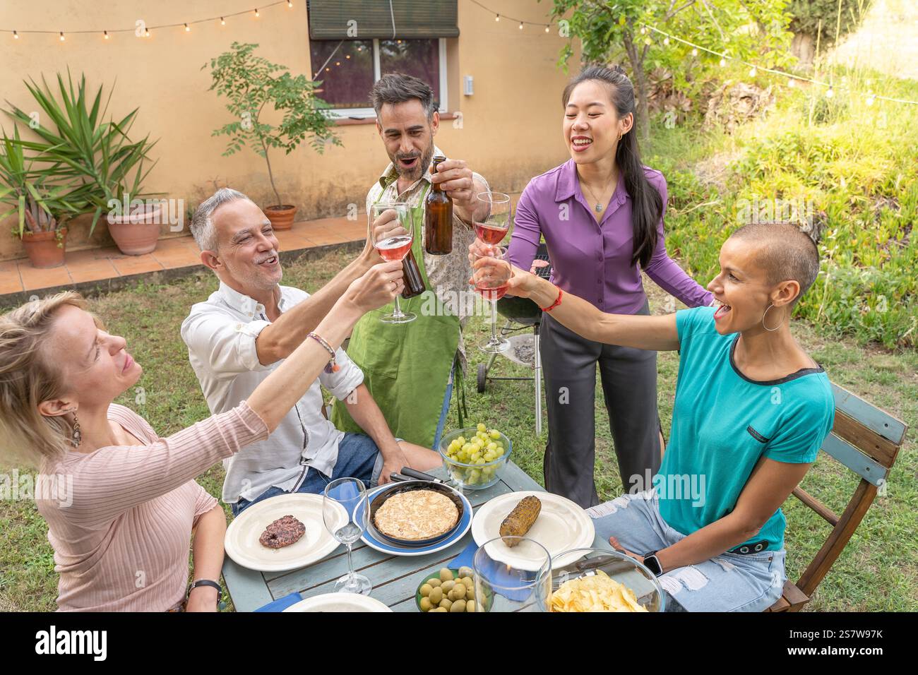 Amis multiraciaux toast avec grand sourire autour de la table au restaurant patio de la maison. Banque D'Images