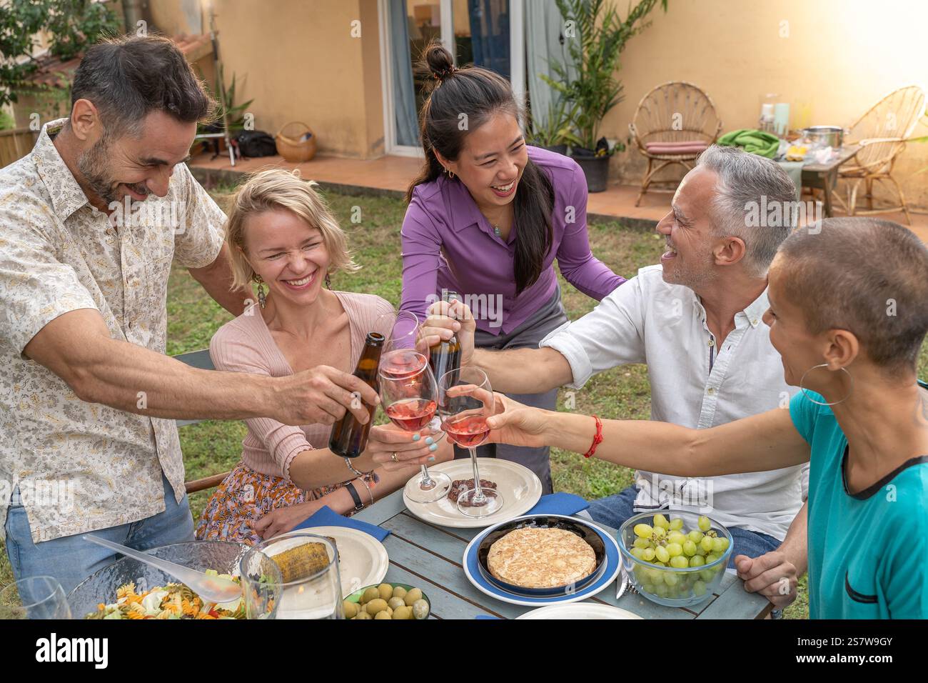 Amis joyeux multiethniques toast avec beau sourire autour de la table au patio de la maison diner. Banque D'Images