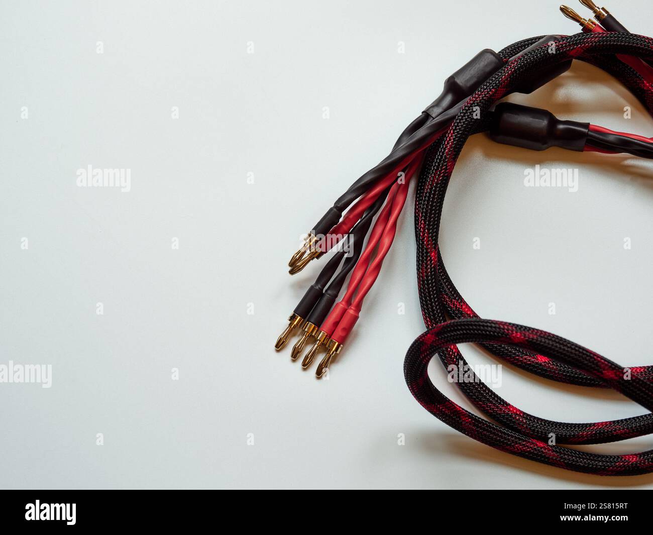 Gros plan de câbles audio avec motif tressé rouge et noir sur un fond Uni. Banque D'Images