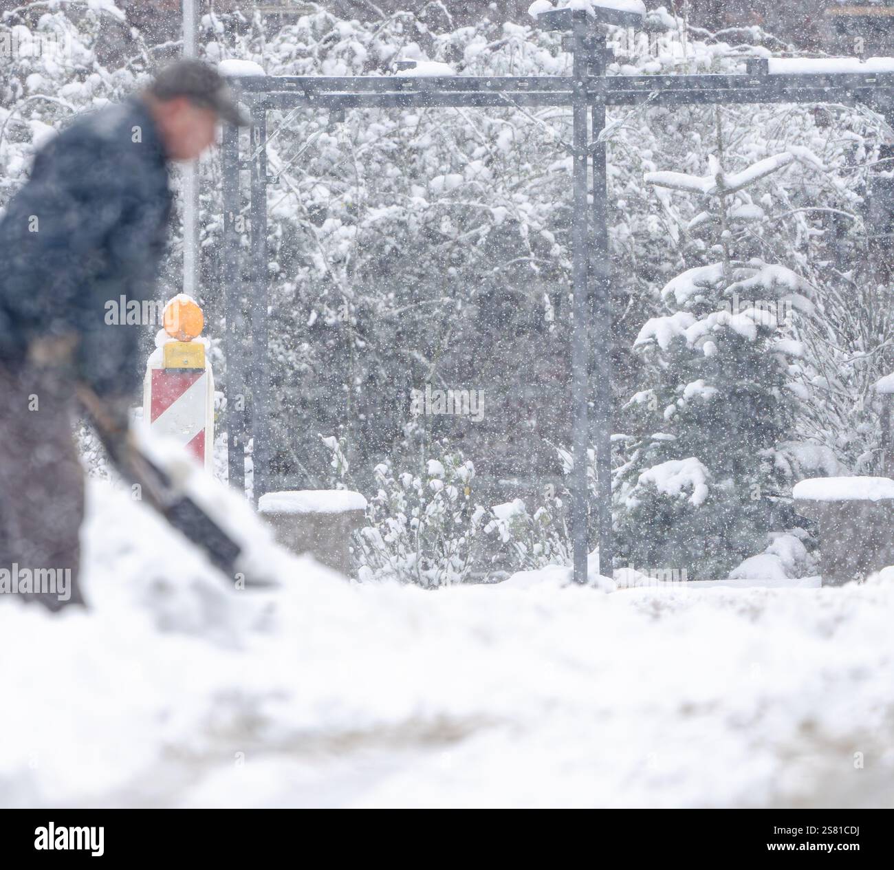 Un homme pelle la neige sur le trottoir. La neige est entassée sur le sol et l'homme utilise une pelle pour la nettoyer. La scène est froide et enneigée Banque D'Images