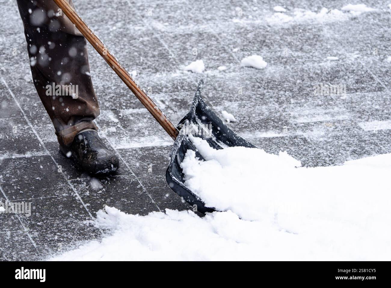 Un homme pelle la neige avec un chasse-neige. La neige est entassée sur le sol, et l'homme utilise une pelle pour la nettoyer. Concept de dur labeur Banque D'Images