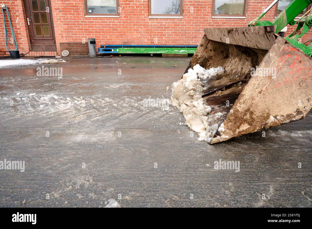 Une pelle est utilisée pour déneiger un trottoir. La pelle est grande et a beaucoup de neige dessus. La scène se déroule dans une ville, avec un buildi de briques Banque D'Images