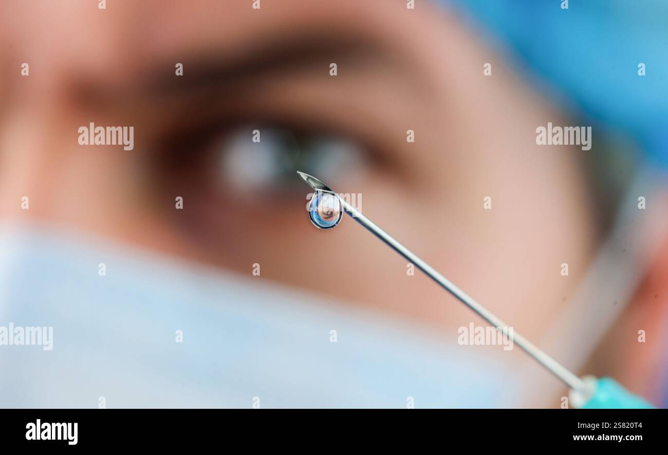 Gros plan d'une goutte de médicament liquide ou de médicament sur l'aiguille de la seringue. Vaccination. Docteur en masque médical avec seringue pour injection. Goutte de médicament sur Banque D'Images