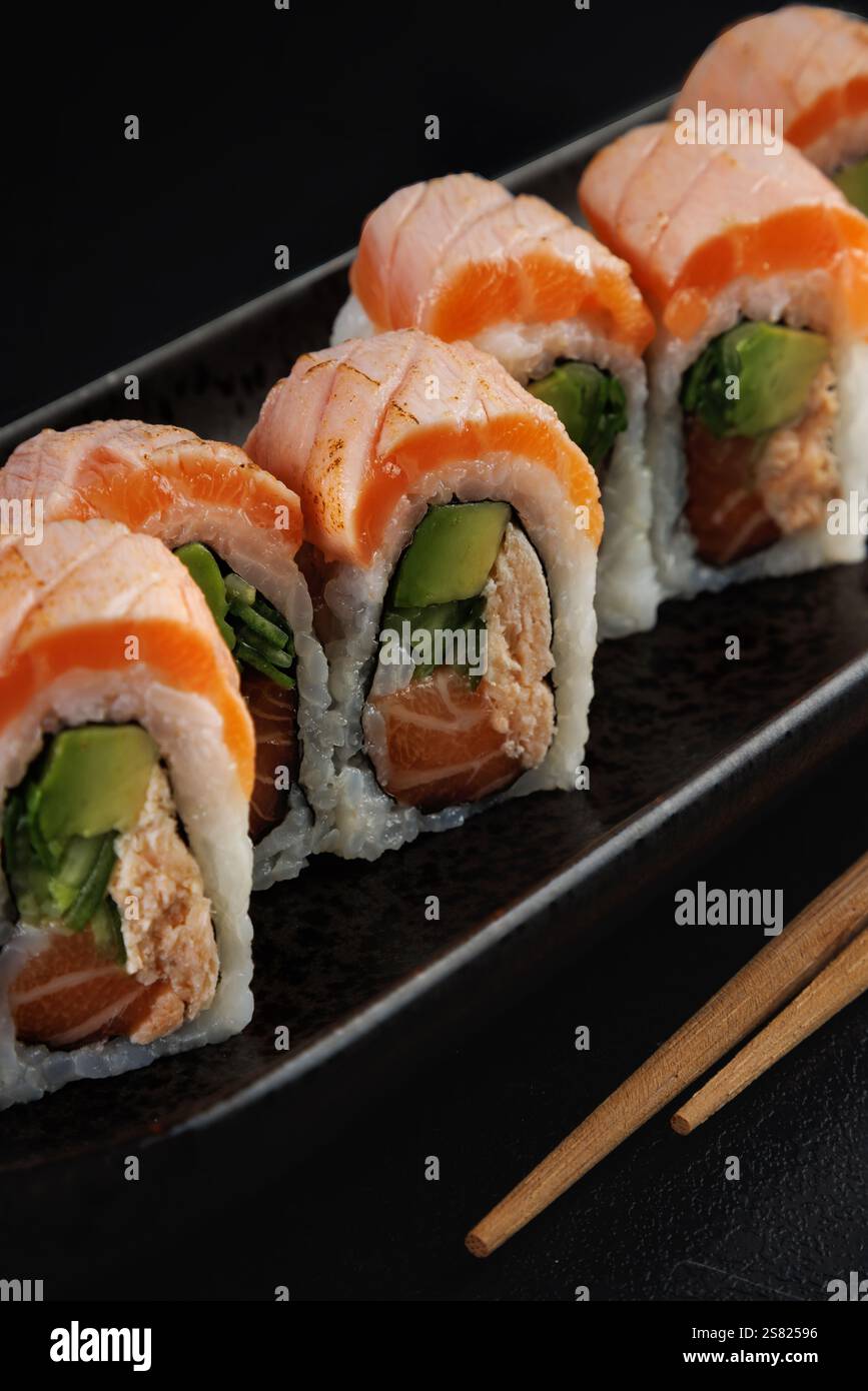 Gros plan de rouleaux de sushi au saumon sur une assiette noire avec des baguettes Banque D'Images