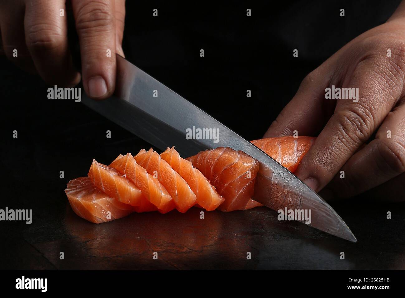 Un chef tranchant le filet de saumon frais avec un couteau japonais pointu, mettant en valeur la précision et la technique sur un fond sombre. Banque D'Images