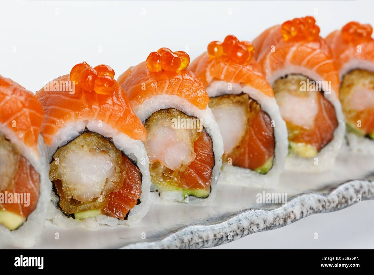 Rouleau de sushi garni de tranches de saumon frais et d'œufs de saumon, rempli de tempura de crevettes, d'avocat et de riz, créant un plat vibrant et délicieux. Banque D'Images