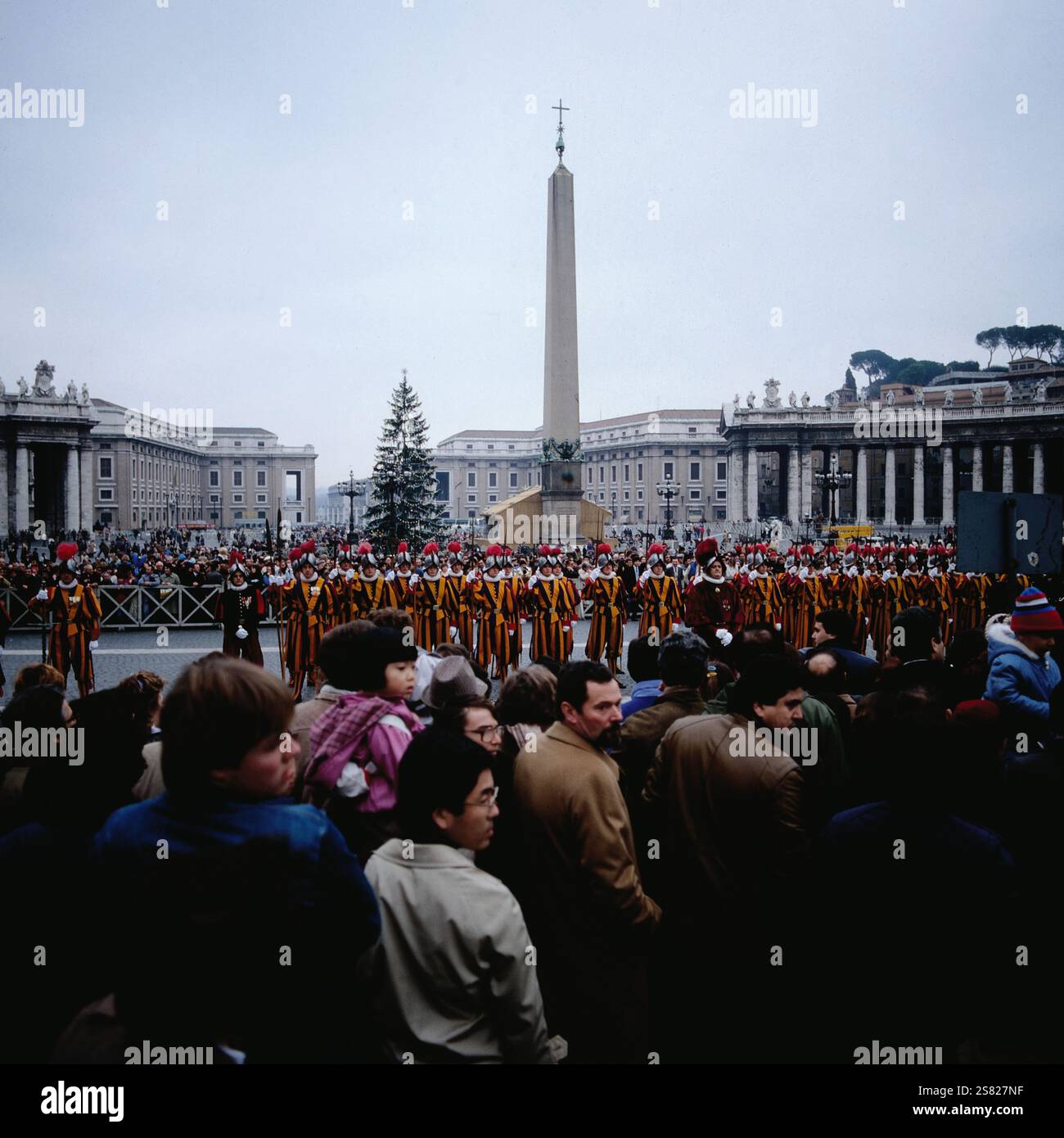 Menschenmenge beobachtet Schweizer Wachen, die in formation auf dem Petersplatz mit Vatikan-Obelisk und Weihnachtsbaum stehen, Italien um 1977. Banque D'Images
