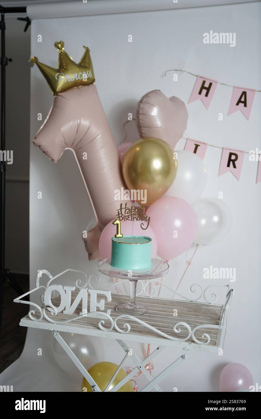 Une configuration de célébration de premier anniversaire avec un gâteau d'anniversaire sarcelle avec des accents dorés, un topper «joyeux anniversaire», et une bougie numéro 1 sur un gâteau en verre Banque D'Images